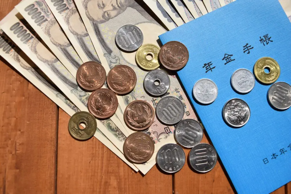 Blue Japanese pension book with yen coins and notes, showing the 20.42 percent tax withheld from a pension lump-sum
