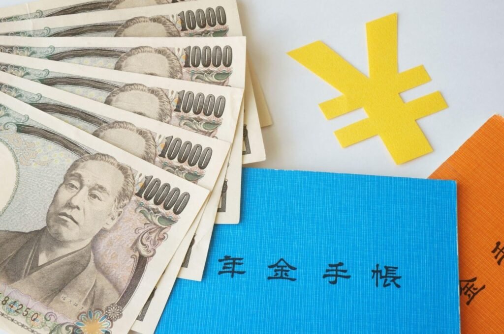 Blue and orange Japanese pension handbooks (nenkin techo) beside a fan of 10,000 yen banknotes and a yellow yen symbol